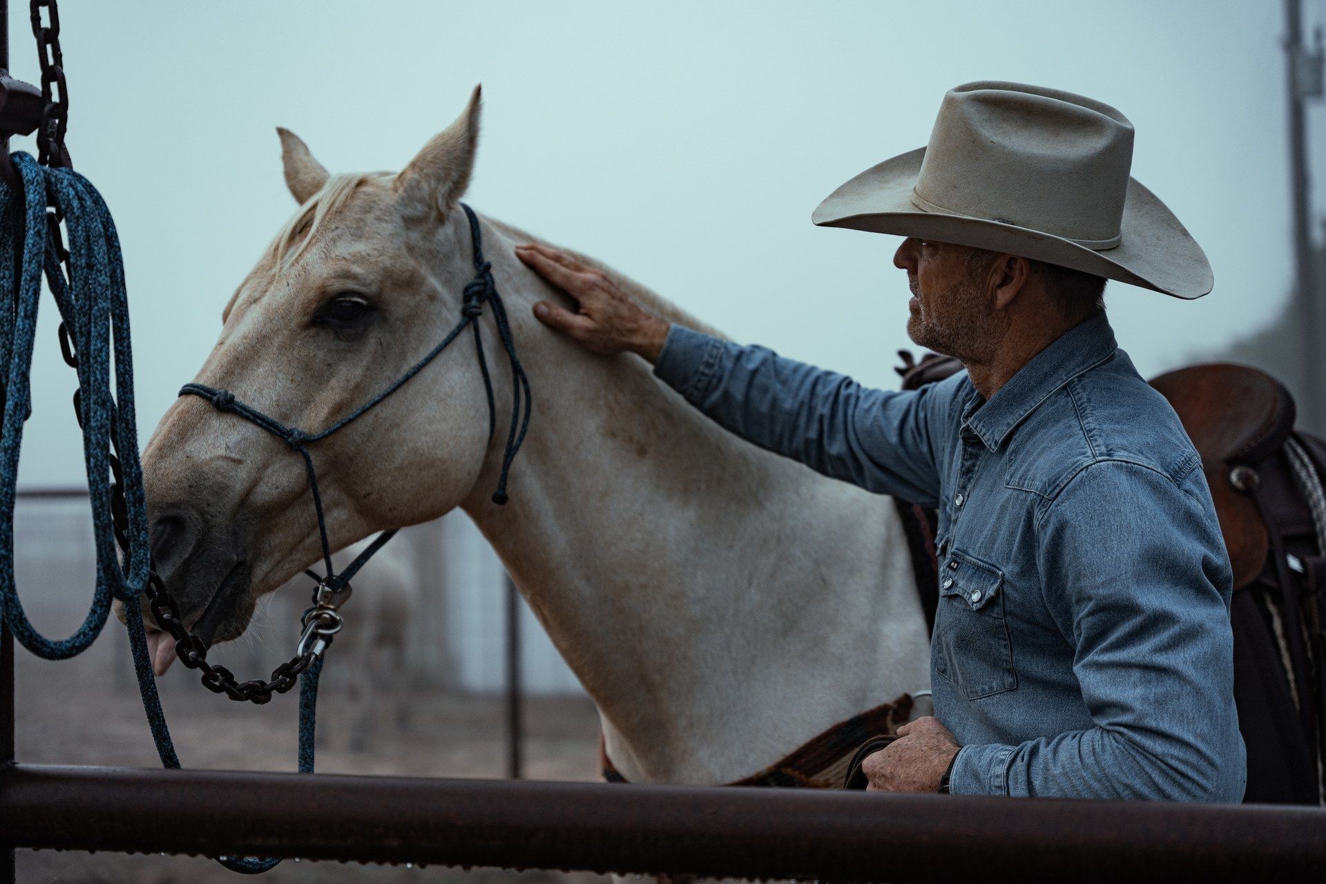 Cowboy in a hat resting his hand on a palomino horse at Oak Hills Ranch.